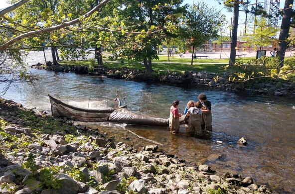 students stand in a creek near a large net