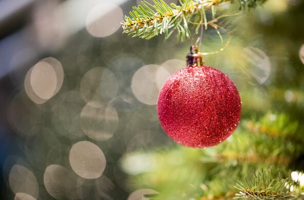 A sparkly red ornament hanging on a Christmas tree