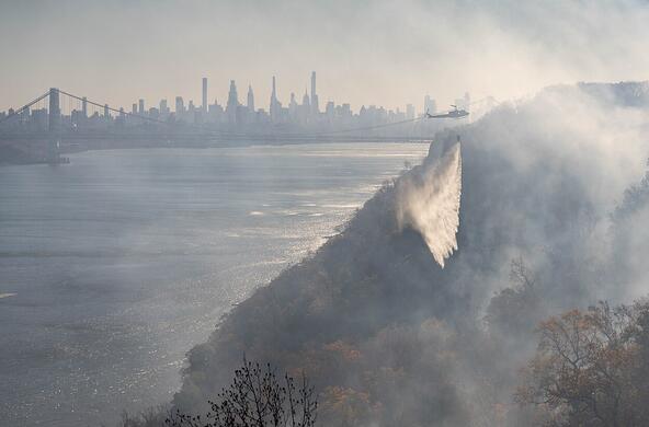 firefighting helicopter flies over smoky Englewood cliffs in New Jersey, with Manhattan skyline in the background