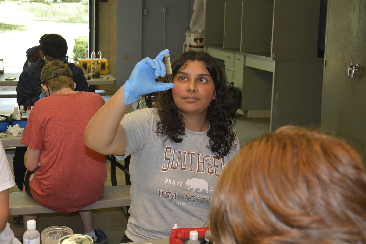 student wearing plastic glove holds up a test tube with soil in it